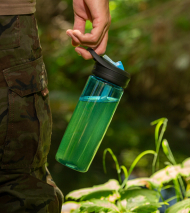 Photo of person with only partial leg and hand visible, holding a water bottle with green liquid.